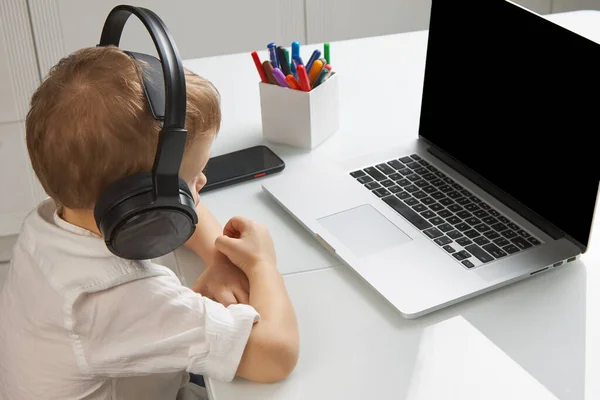 Ένα παιδί με ακουστικά κοιτάζει προσεκτικά την οθόνη του φορητού υπολογιστή. — Φωτογραφία Αρχείου