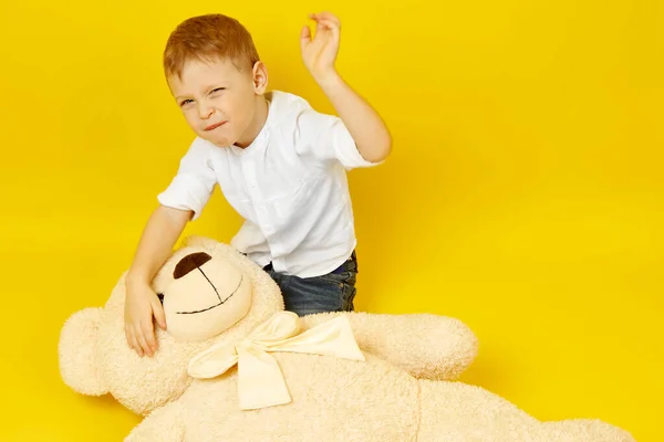 Розчарований маленький хлопчик вдарив плюшевого ведмедя на жовтому тлі . — стокове фото