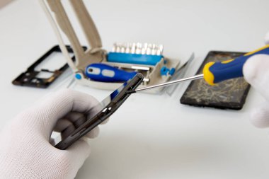 Parçalanmış akıllı telefon ve tamir araçları: cımbız ve tornavida.