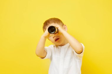 Mutlu bir çocuk sarı arka plandaki teleskoptan bakar.