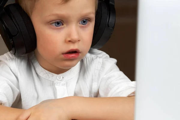 Αγόρι που φοράει ασύρματα ακουστικά, κάθεται σε ένα γραφείο, χρησιμοποιώντας ένα φορητό υπολογιστή — Φωτογραφία Αρχείου