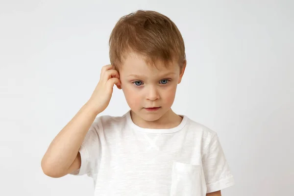 Маленький мальчик погружен в мысли и чешет голову на белом фоне. — стоковое фото