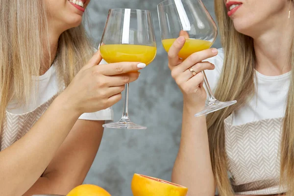 Две милые блондинки пьют алкогольный коктейль на кухне и едят свежие фрукты. — стоковое фото