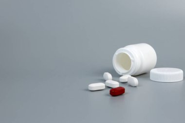 Gri arka planda dağınık haplarla dolu beyaz bir kavanoz.