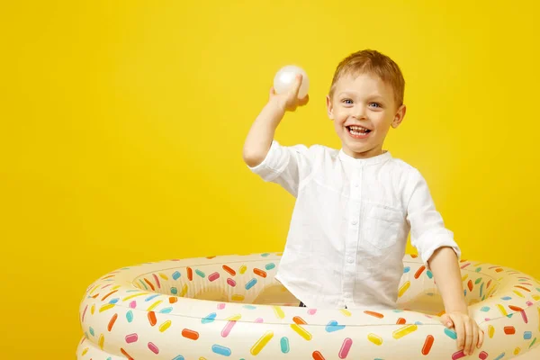 Un pequeño niño sonriente juega en una piscina seca sobre un fondo amarillo. — Foto de Stock