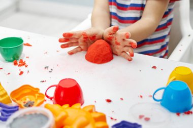 Bir çocuğun elleri beyaz bir masada parlak kinetik kumla oynar. Parlak kalıpların kullanıldığı eğitici bir kinetik kum oyunu