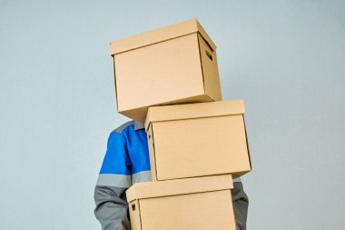 Bir yükleyici ya da kurye, iş kıyafetleri içinde mavi duvar boyunca karton kutular taşır. Taşınma günü. Online mağazadan mal teslimatı.