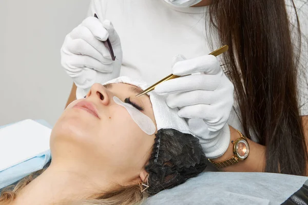 The master of eyelash extension uses tweezers to fix the eyelashes.