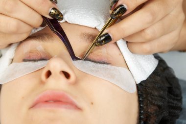 Kirpik uzatma uzmanı kırbacı sağlamlaştırmak için cımbız kullanır. Kirpikleri artırmak için bir kozmetik prosedürü yakın plan