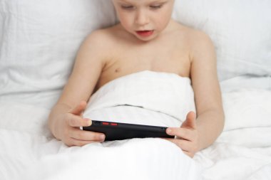 Cep telefonu, yatakta oturan küçük bir çocuğun elinde.