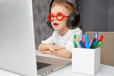 Kırmızı gözlüklü ve kulaklıklı şirin çocuk bilgisayar kullanarak internet üzerinden iletişim kurarken eğleniyor. Uzaktan iletişim ve modern iletişim kavramı