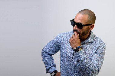 Siyah güneş gözlüklü düşünceli Latin adam, beyaz arka planda izole edilmiş fotokopi odasına bakıyor ve düşünüyor.