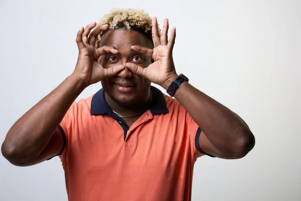 Retrato de un hombre negro mirando a través de sus dedos a través de binoculares sobre un fondo blanco — Foto de Stock