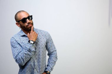 Siyah güneş gözlüklü düşünceli Latin adam, beyaz arka planda izole edilmiş fotokopi odasına bakıyor ve düşünüyor.