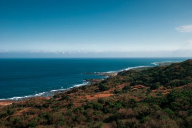 Bir dağın tepesinden mavi denizin panoramik manzarası. Güneşli bir gün ve açık mavi bir gökyüzü uzun bir kıyı şeridi boyunca uzanır..