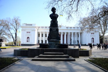 ODESSA, UKRAINE - 20 Nisan 2019: Rus şair ve yazar Alexander Puşkin anıtı, Ukrayna bayrağı, saat, heykel ve tüm ayrıntılarıyla Odessa belediye binasının arkasında