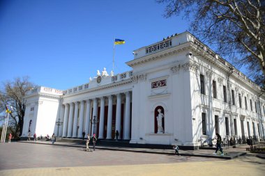 ODESSA, UKRAINE - 20 Nisan 2019: Rus şair ve yazar Alexander Puşkin anıtı, Ukrayna bayrağı, saat, heykel ve tüm ayrıntılarıyla Odessa belediye binasının arkasında