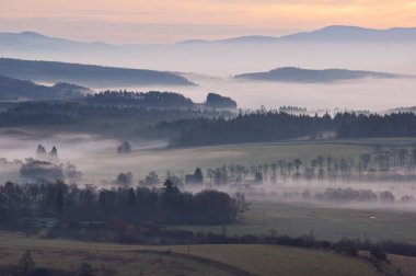 Sakin kırsal alanlarda sisli bir sabah manzarası ve uzak evler. Sakin bir kır manzarası sisli bir sabahı tarlalarda yuvarlanırken yakalıyor. Uzaktan bakan evler sislerin arasından sakin ve huzurlu bir atmosfer yaratıyor.. 