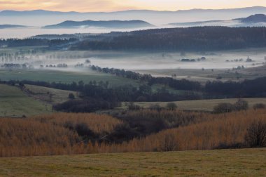 Sakin kırsal alanlarda sisli bir sabah manzarası ve uzak evler. Sakin bir kır manzarası sisli bir sabahı tarlalarda yuvarlanırken yakalıyor. Uzaktan bakan evler sislerin arasından sakin ve huzurlu bir atmosfer yaratıyor.. 