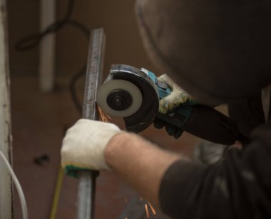 İspanyol açı öğütücü diski döndürür, bir insan elleriyle metal profili keser, kıvılcımlar uçuşur, güzel parıltı, bokeh, siyah arkaplanda turuncu ışık, prodüksiyon, flaş ışık