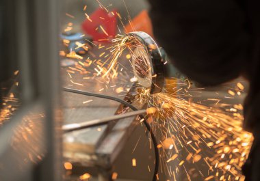 İspanyol açı öğütücü diski döndürür, bir insan elleriyle metal profili keser, kıvılcımlar uçuşur, güzel parıltı, bokeh, siyah arkaplanda turuncu ışık, prodüksiyon, flaş ışık