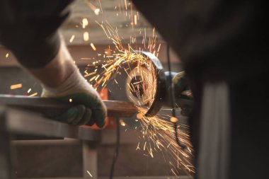 İspanyol açı öğütücü diski döndürür, bir insan elleriyle metal profili keser, kıvılcımlar uçuşur, güzel parıltı, bokeh, siyah arkaplanda turuncu ışık, prodüksiyon, flaş ışık