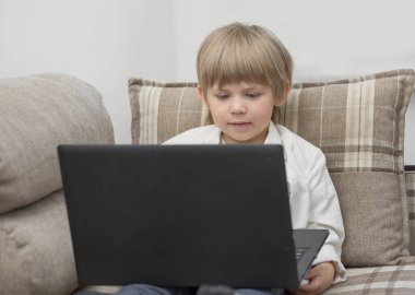 Çocuk kucağında dizüstü bilgisayarla kanepede oturur ve ekrana bakar.
