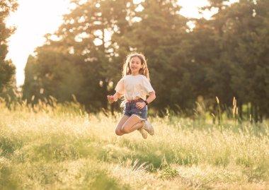 Mutlu genç kız gün batımında bir tarlaya atlar. Yazın çocuk eğlencesi konsepti