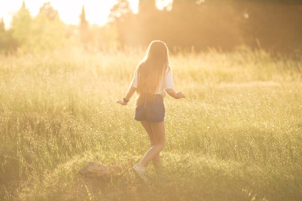 a teenage girl runs through a field of tall grass in the rays of the setting sun