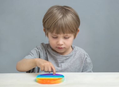 Çocuk masada oturur ve silikon oyuncak anti-stres popit çalar.