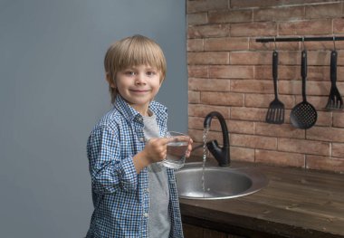 Bir çocuk musluktan mutfaktaki bir bardağa su döküyor. iyi su kavramı