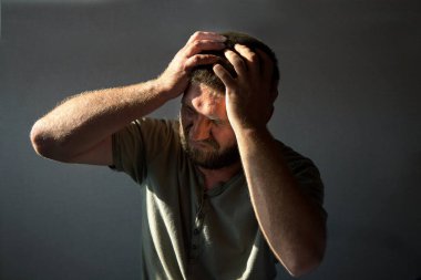 Genç bir adamın yakın plan portresi, acı çekiyor ve başını tutuyor. Akşamdan kalma, baş ağrısı ya da hastalık konsepti