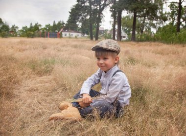 Antika elbiseli bir çocuk, kuru otlarla dolu bir tarlada oturuyor, kırsal bir alanda.