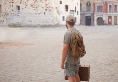 Sakallı bir adam antika bir şehirde eski bir sırt çantası ve bavuluyla duruyor. Seyahat konsepti. Boşluğu kopyala