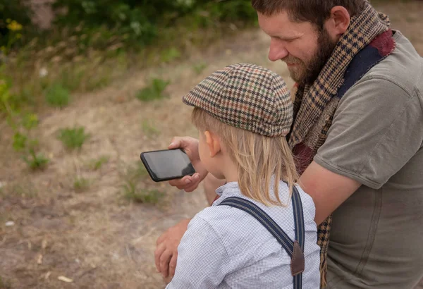 dad teaches his son to take pictures on the phone, they are in nature