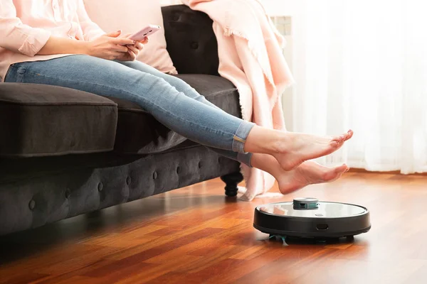 Yerleri temizlemek için elektrikli süpürge kullanan, akıllı makine ev işi robotu kontrol eden genç bir kadının yüzsüz orta bölümü.