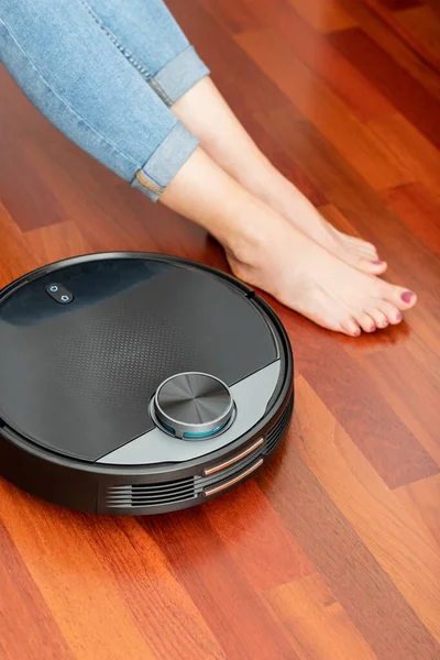 Young girl feet when a round smart automatic vacuum cleaner passes to clean the floor, controlling machine housework robot