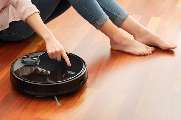 Yerleri temizlemek için elektrikli süpürge kullanan, akıllı makine ev işi robotu kontrol eden genç bir kadının yüzsüz orta bölümü.