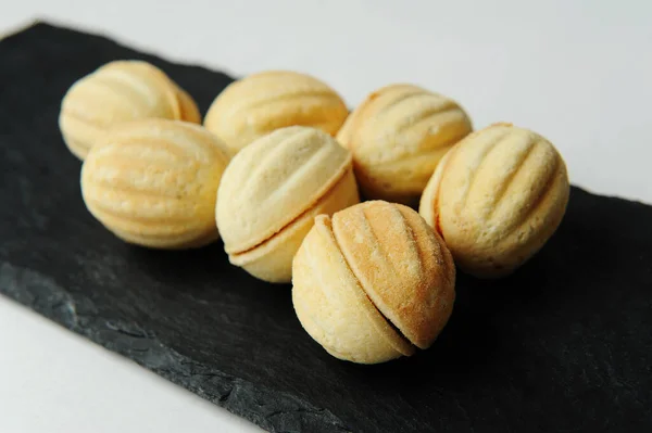 Galletas en forma de nuez con leche condensada hervida. pizarra negra, fondo blanco, primer plano —  Fotos de Stock