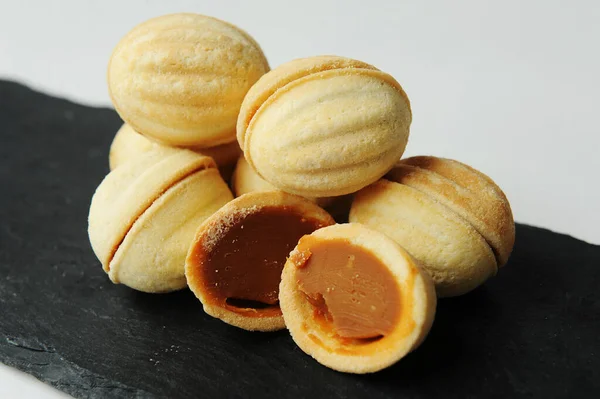 Galletas en forma de nuez con leche condensada hervida. pizarra negra, fondo blanco, primer plano —  Fotos de Stock