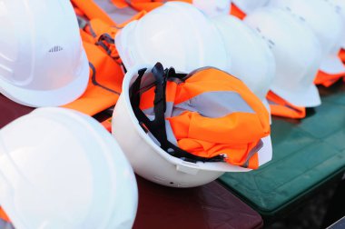 İnşaat alanında beyaz miğfer ve turuncu yelek setleri var, insan yok.