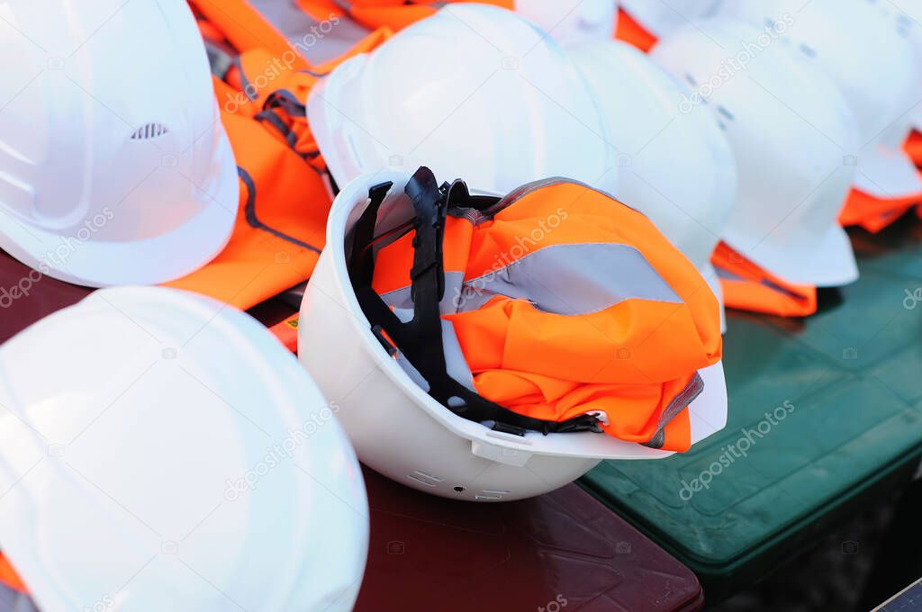 Sets of white construction helmets and orange vests at a construction site, no people