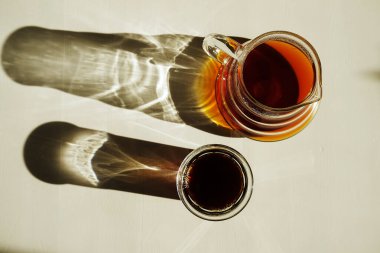 Üçüncü dalga özel kahve estetiği. Kahvenin üzerine taze demlenmiş siyah kahve, güneş ışığıyla aydınlanmış beyaz masada bir sürahi ve bardakta servis edilir. Üst manzara, güzel gölgeler