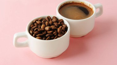 Kahve çekirdekleri ve siyah espresso pembe arka planda iki beyaz fincanda.