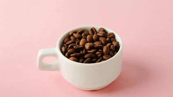 Granos de café en taza blanca sobre fondo rosa suave — Foto de Stock