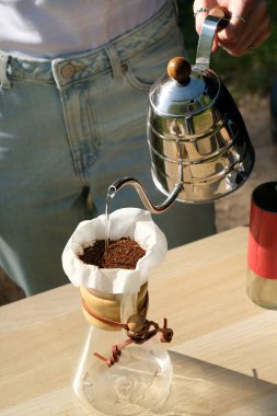 Damlayan kahve demleme işleminin üzerine elle dökülüyor. Kaz boynu çaydanlığından damlatıcıya su dökülüyor. Barista 'nın elleri çerçevede. Kırmızı öğütücü