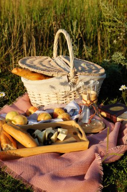 Gün batımında çayırda yaz pikniği. Hasır sepet, baget, peynir, elma, kahve sürahisi
