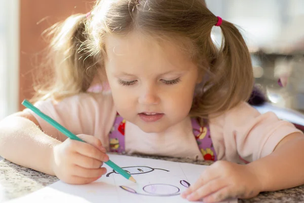 Child draws with a pencil and smiles.