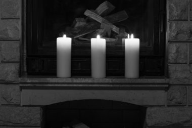 Şöminenin üzerinde duran beyaz büyük mumlar. 