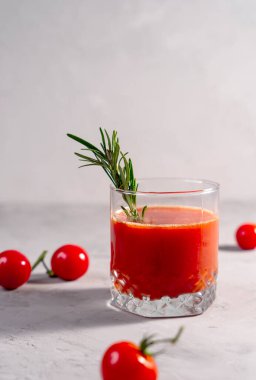 Faydalı içecek, kiraz domatesleri ve domates suyu gri arka planda biberiye dalı olan bir bardakta, dikey fotoğraf.